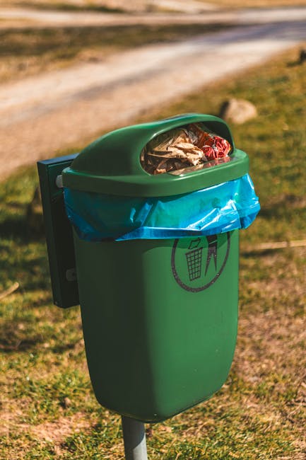 A crumpled, transparent plastic water bottle with a white and blue cap lies discarded on a patch of green grass. The bottle shows creases and folds indicative of being squeezed or crushed, and partial